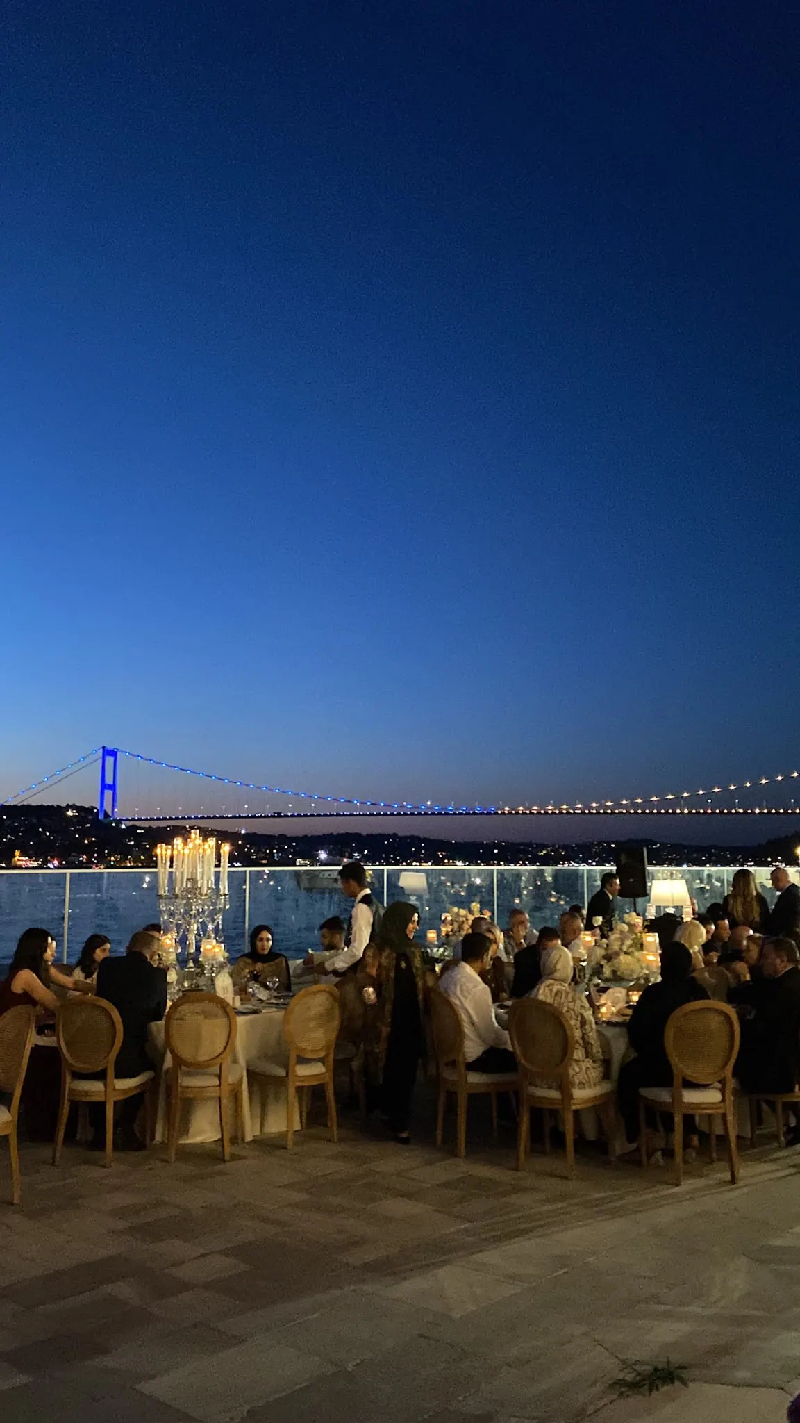 Boğaz Köprüsü manzaralı gece düğününde yuvarlak masalar ve ahşap madalyon sandalyeler