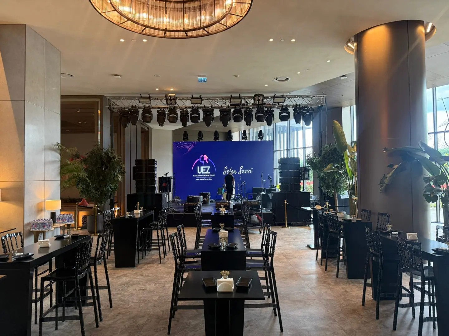 UEZ 2026 konferans salonunda siyah bistro masa, yüksek sandalye ve sahne düzeni